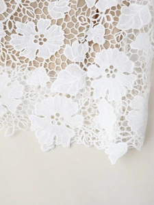 Gros plan détaillé sur les motifs de dentelle florale blanche avec doublure beige sur la robe