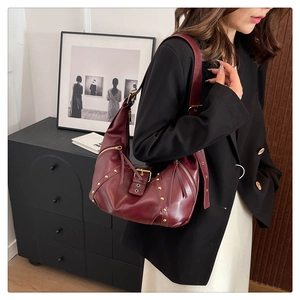 Detail of burgundy half-moon bag with gold studs and adjustable strap on a model