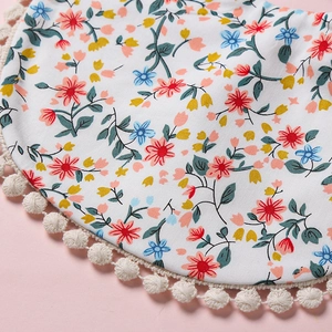 Détail d'un bavoir floral pour bébé avec bordure pompon blanc et texture coton sur fond rose