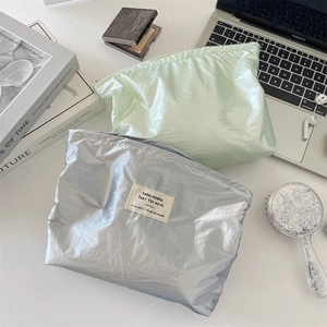 Detail of silver and mint green makeup bags with metallic texture and zipper on a desk