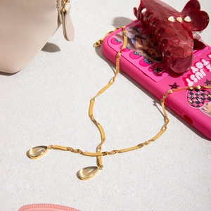 Golden snake chain necklace with dual clear teardrop pendants on a white beach