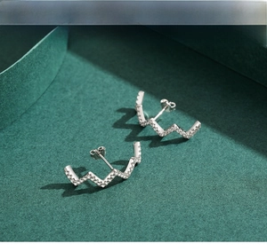 Macro shot of silver wave earrings with sparkling zircon pave on a textured background