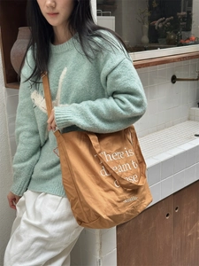 Brown canvas tote bag with adjustable shoulder strap and white typography on front