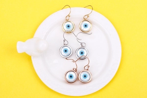 Detailed view of evil eye earrings in gold, silver and rose gold on white ceramic tray