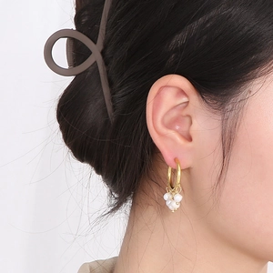 Detailed close-up of a gold hollow earring with cluster white pearls on a model