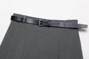 Detail of grey pleated skirt waist with a black crocodile pattern faux leather belt