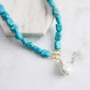 Baroque pearl necklace with turquoise stones and golden floral detail on marble
