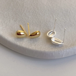 Close-up of minimalist gold and silver teardrop stud earrings on a textured base