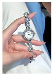 Détail de montre argentée pour femme avec bracelet perles et lunette en strass