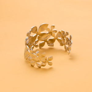 Close-up of a silver flower-shaped open cuff bracelet on a vibrant orange background