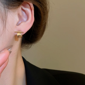 Macro side view of minimalist gold geometric stud earrings on model's ear with polished finish