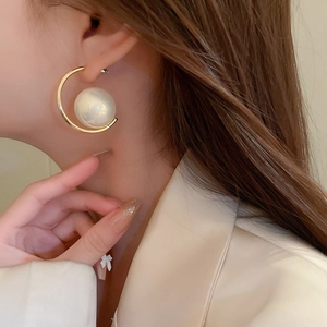 Close-up of golden C-shaped hoop earrings with a large white pearl on model ear
