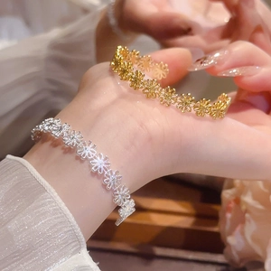 Detailed view of hollow flower bangles in gold and silver finish on a model's wrist