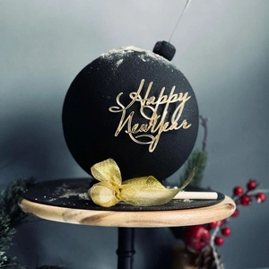 Close-up of Happy New Year cake topper with golden bow on round black textured ornament