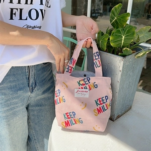 Pink corduroy handbag with Keep Smiling print and magnetic clasp on a white table