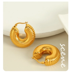 Close-up of golden hollow hoop earrings with textured ripple surface and snap closure