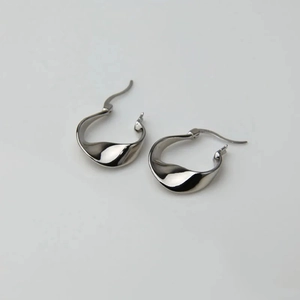 Macro shot of silver-colored irregular twisted wave hoop earrings with polished finish
