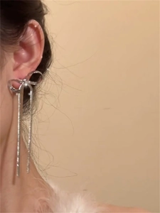 Close-up of silver bow earrings with long snake chain tassels on model's ear