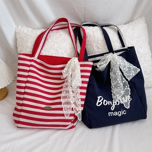 Detail of canvas tote bags with lace bows in red stripes and navy blue with magic text