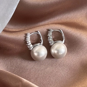 Detailed view of silver pearl hoop earrings with zircon accents on soft silk fabric