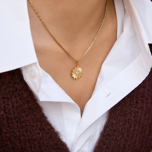 Dettaglio del ciondolo a sole dorato con diamante a cuore su una collana a catena a fune