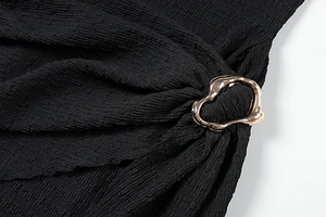 Détail d'une robe en tissu plissé noir avec une boucle anneau en métal doré unique