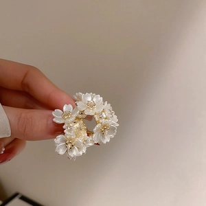 Detailed macro shot of white floral hair claw clip with golden beads and rhinestones