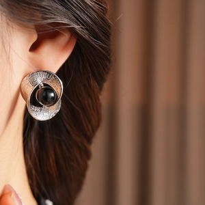Close-up of twisted silver textured metal earring with a black round bead on a model
