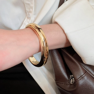 Gros plan d'un large bracelet manchette en or poli porté par un mannequin en mode lifestyle
