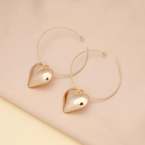 Detail shot of gold-plated hoop earrings with 3D heart pendants on soft fabric background