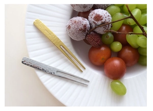Macro shot of gold and silver fruit forks with hammered texture on a plate with fresh fruits