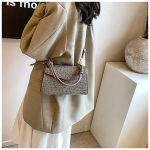 Detail showing grey crocodile pattern leather handbag with twisted handle and gold hardware