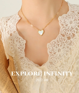 Close-up of gold paperclip chain necklace with a white shell heart pendant on a model