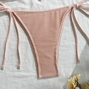 Detail of pink waffle texture bikini bottoms with adjustable side ties on white fabric