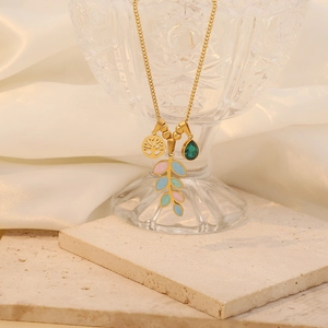 Detail of gold necklace with tree of life charm, green crystal, and enamel leaf pendant