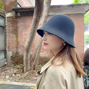 Vue latérale d'un chapeau cloche en feutre de laine noir porté contre un mur de briques