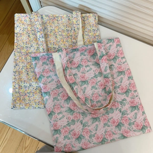 Floral print canvas tote bags in pink rose and yellow wildflower patterns on white surface