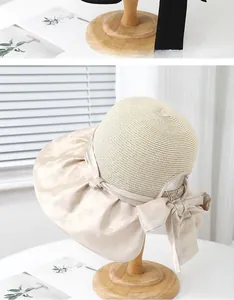 Detail of wide-brimmed straw hat featuring fine weave and elegant silk bow on wooden stand