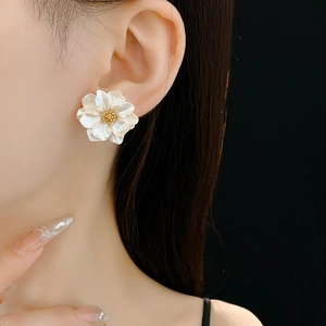 Close-up of matte white flower stud earrings with gold bead centers on a model