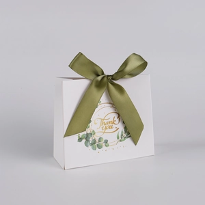 Close-up of white wedding favor box with green ribbon and gold Thank You lettering
