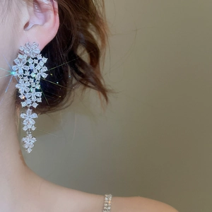 Close-up of dangling flower tassel earrings with zircons on model against yellow background