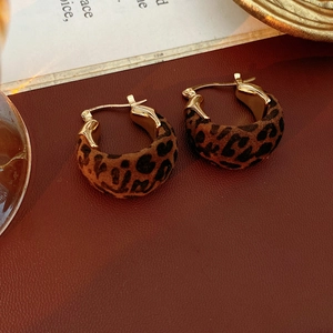 Dettaglio degli orecchini a cerchio dorati a forma di U con motivo leopardato su cuoio