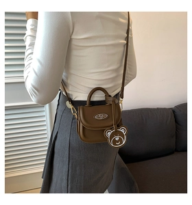 Detail of a dark brown mini crossbody bag with a bear charm and HELLO lettering