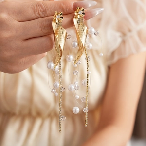 Close-up of golden leaf earrings with shimmering zircon flowers and long pearl tassels