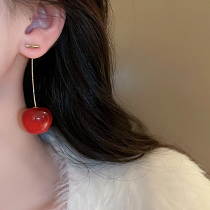 Detail of red resin cherry drop earrings with gold-tone accents worn by a model