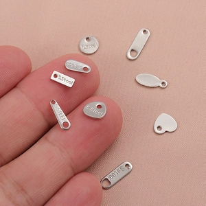 Assorted silver stainless steel heart and oval charms held by hand on pink fabric background