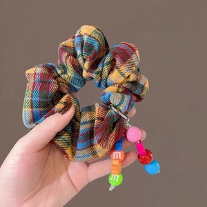 Rainbow plaid scrunchie with colorful letter m beads held against brown backdrop