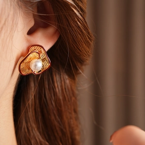 Close-up of gold-plated heart earring with grid texture and pearl worn by a model