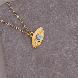 Detail of gold eye pendant necklace featuring a centered blue turquoise stone