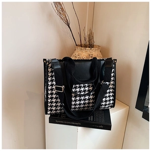 Detail of vintage houndstooth tote bag with black PU leather straps on a minimalist display